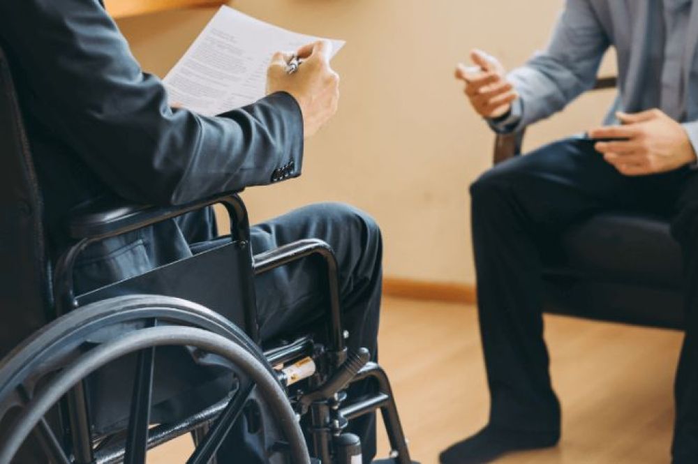 man in wheelchair reviewing documents across from another person talking