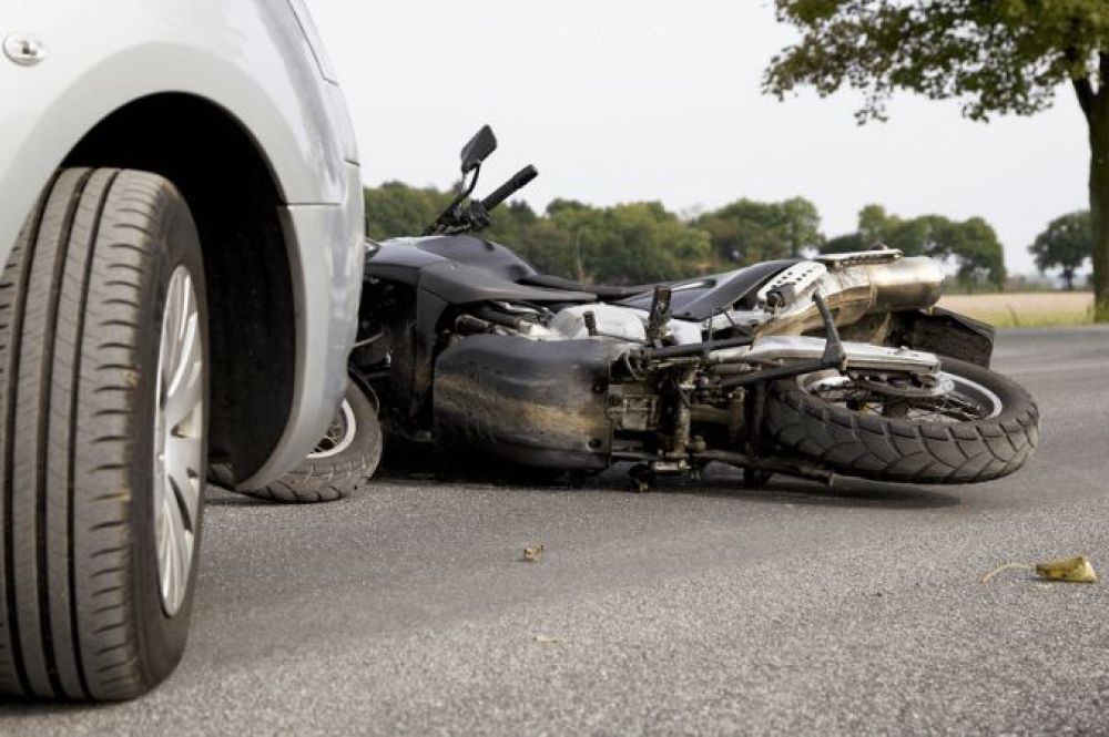 motorcycle on its side in front of car with tree in background