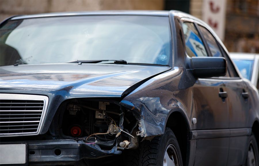 Damaged car with broken headlight and dented fender on street, showing vehicle accident aftermath.