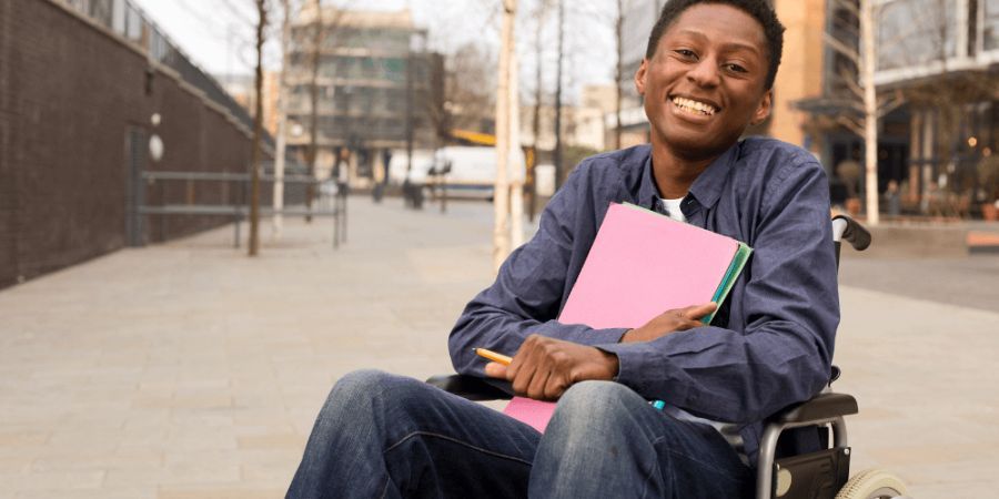 Young man in wheel chair smiling with files in his lap.