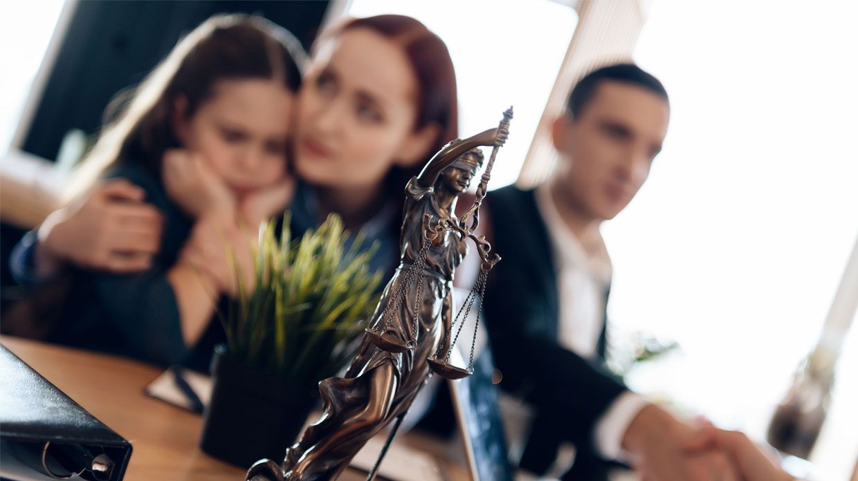 Bronze statue of Themis stands on table, behind which sits divorcing parents with little girl