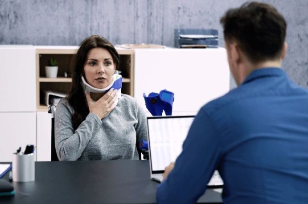 woman in neckbrace meeting with man at desk