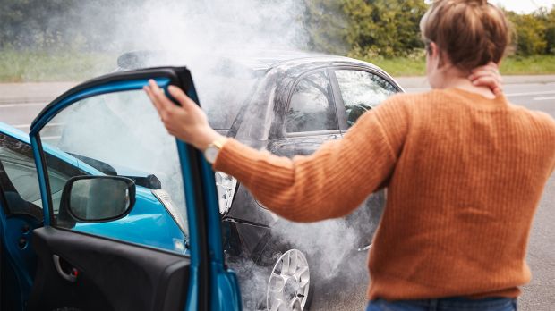 woman holding her neck and getting out of her car after an accident