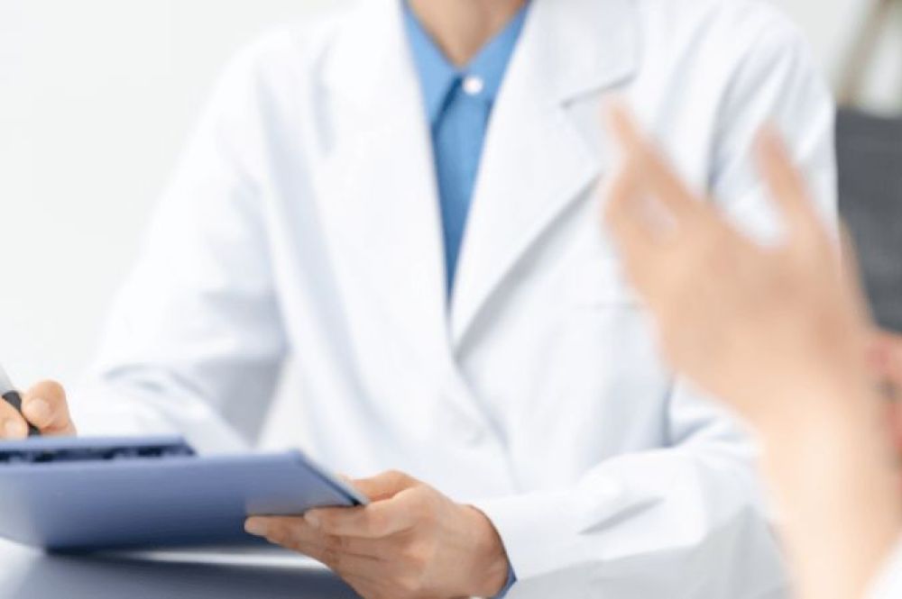 doctor writing on paper while talking to person in foreground