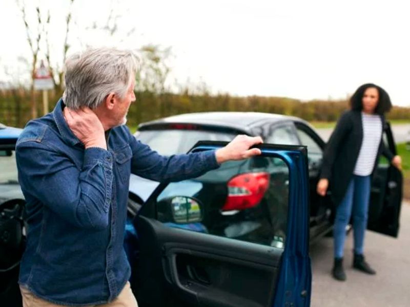 Man holding neck near car, woman approaches after minor accident on the road.