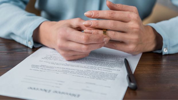 woman taking off wedding ring and divorce decree on table
