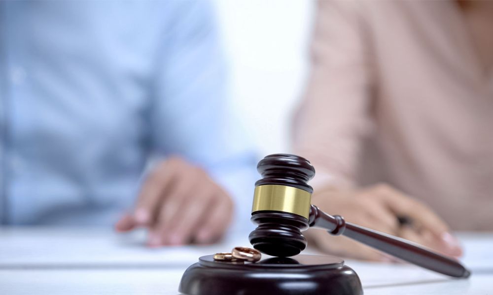 Marriage rings and gavel closeup, spouses signing divorce document on background