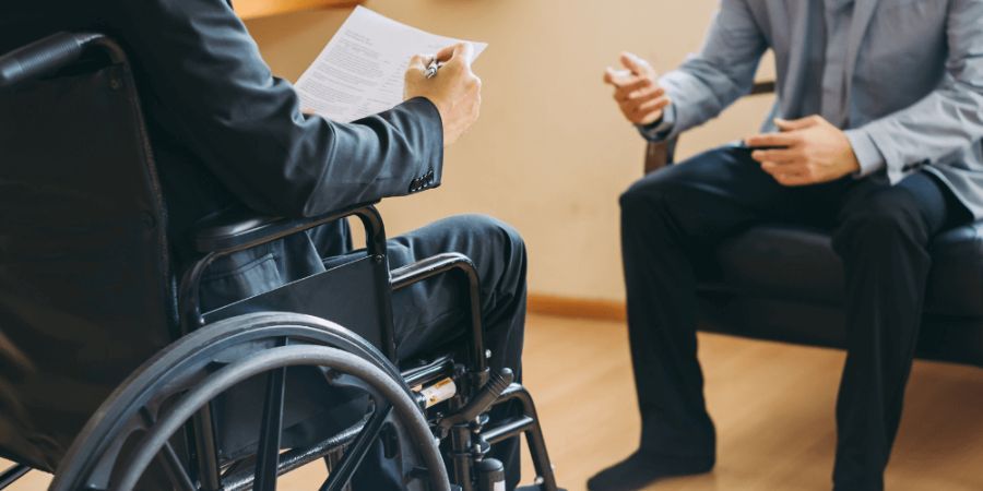 man in wheelchair reviewing documents across from another person talking