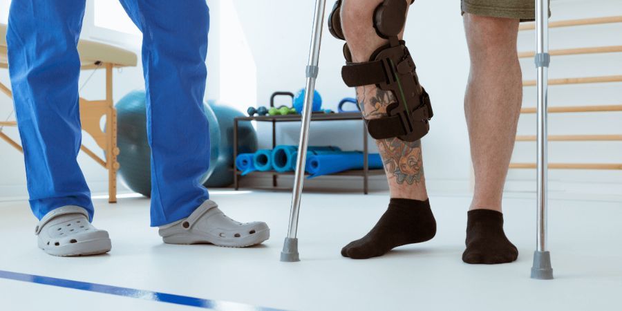 man wearing leg braces and using crutches with doctor assisting him