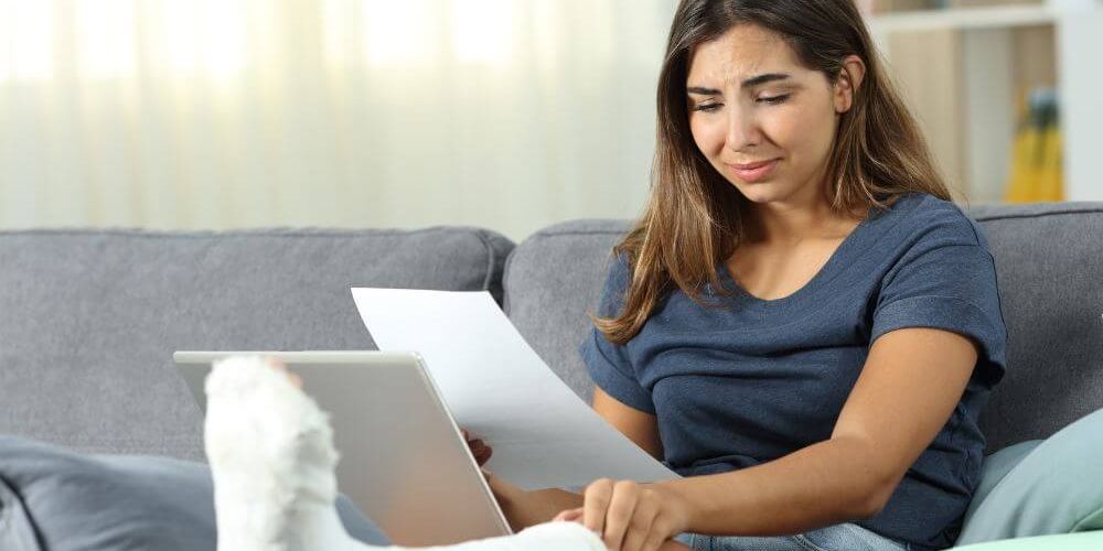 Woman with a leg cast sitting on a sofa, reading a document, looking concerned.