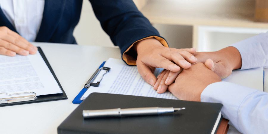 Two people looking at paperwork, one comforting the other with a hand touch