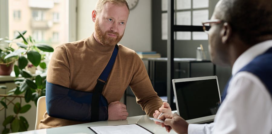 A man with an arm in a sling consults with a professional in an office setting, representing the complexities of personal injury claims involving pre-existing injuries