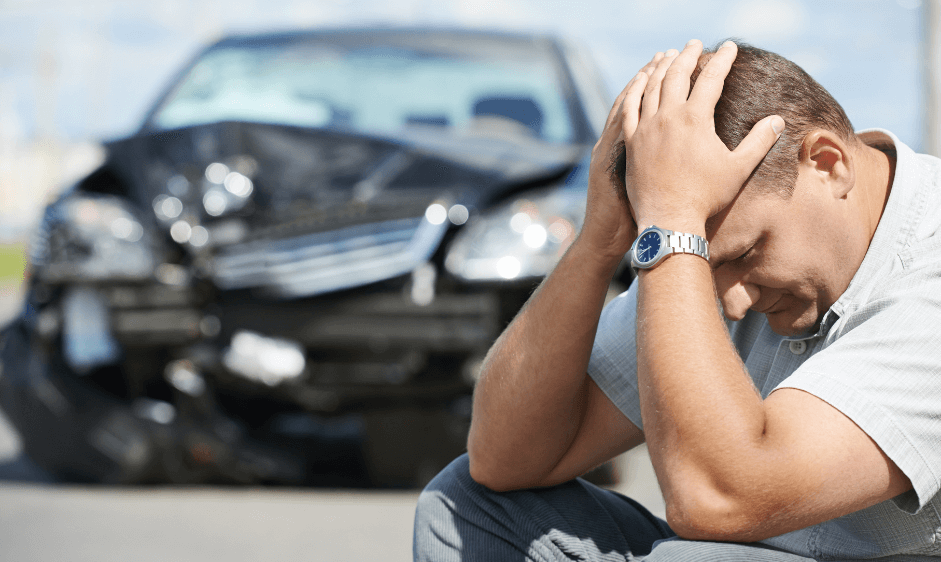 Man holding his head in front of his wrecked car