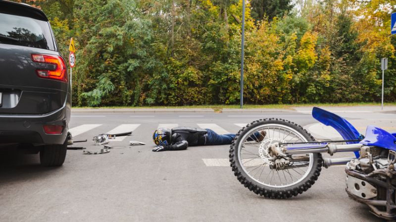 Motorcycle rider laying on the ground next to a motorcycle in the road