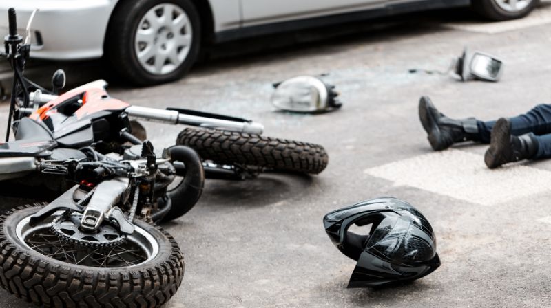 Motorcycle laying on ground next to man
