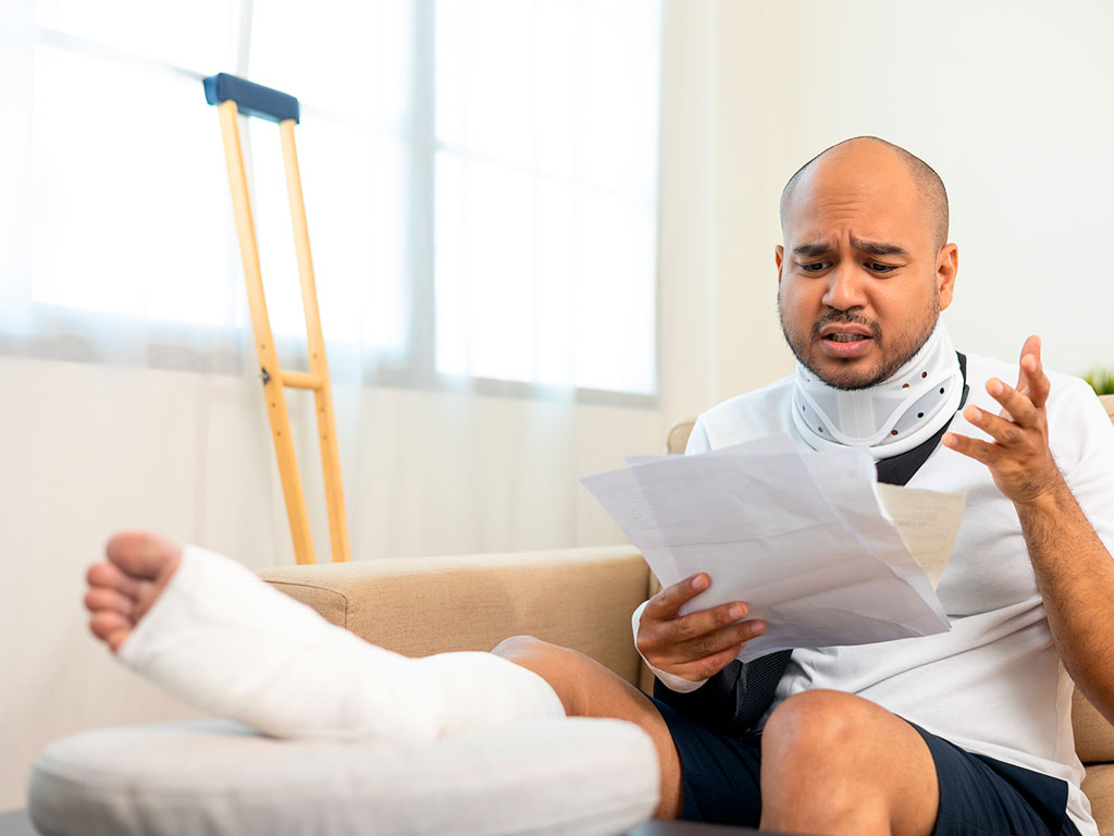 man wearing a leg cast looking distraught at paperwork