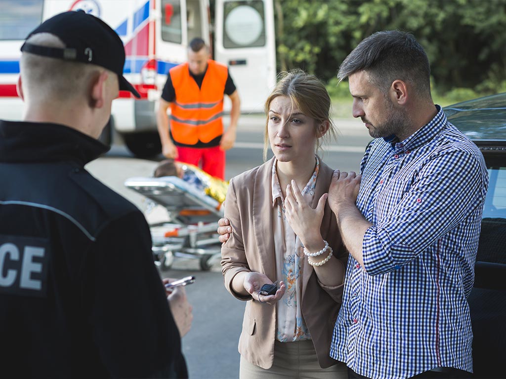 A man and a woman talking to a police officer after a car accident