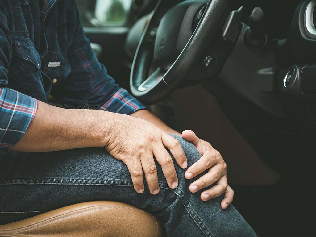 man sitting in his car holding his leg in pain