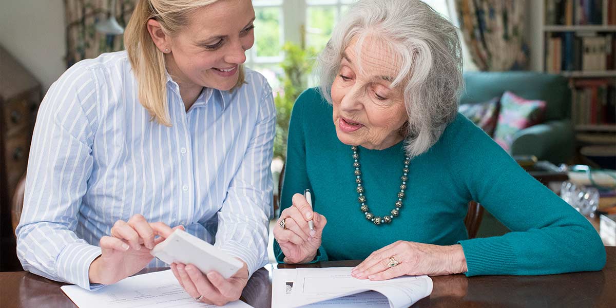 elderly woman receiving help from another woman with her paperwork
