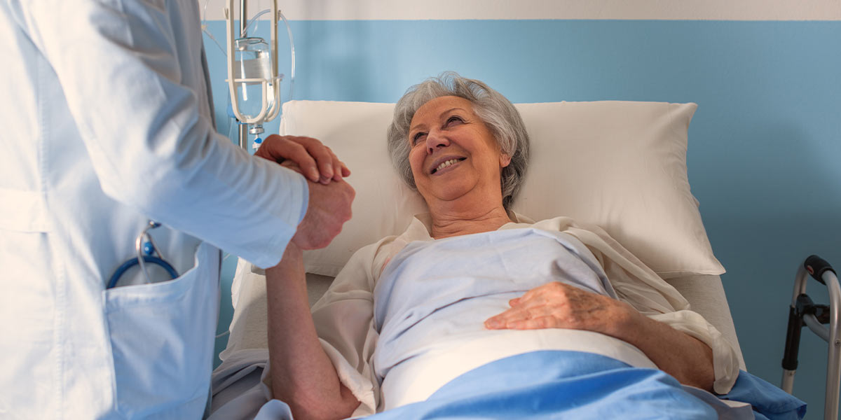 Elderly woman laying in a hospital bed holding a doctors hand
