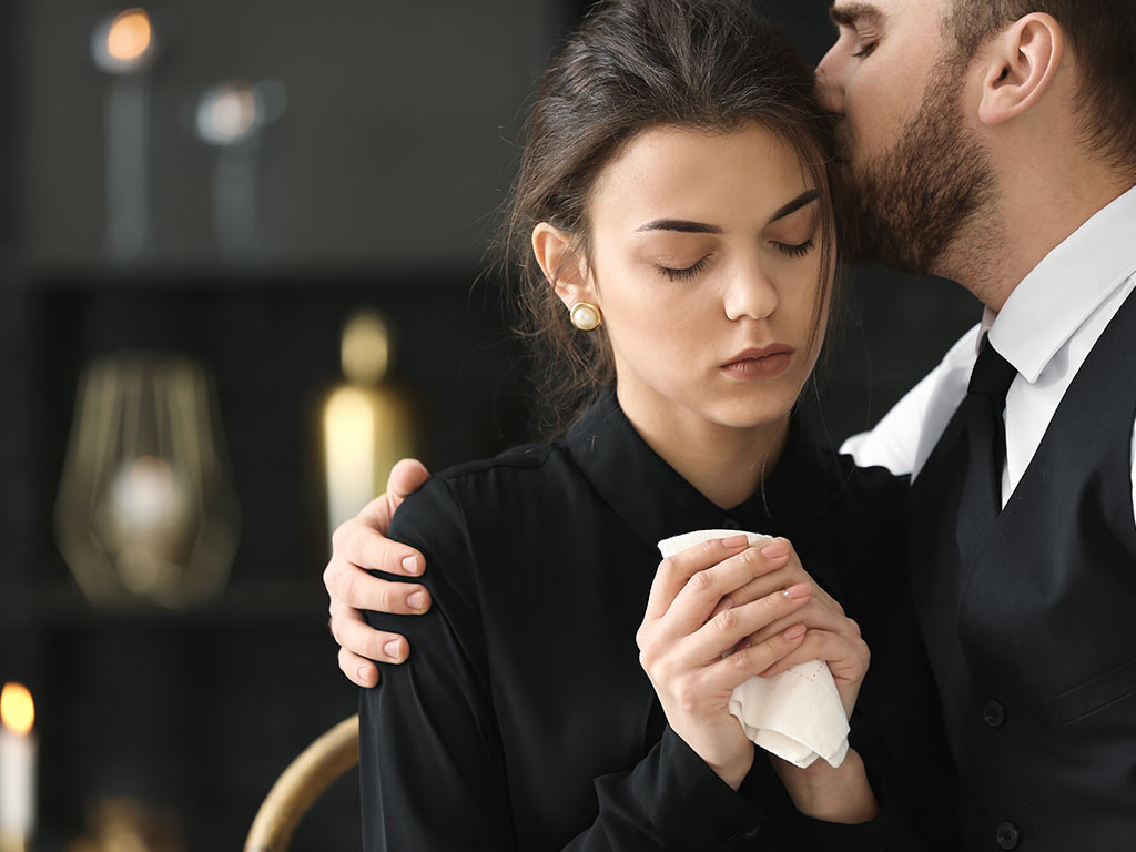 man kissing the side of a grieving woman's head