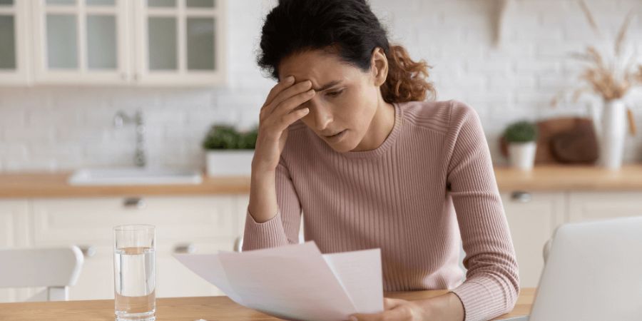 Frustrated woman with hand on forehead looking at paperwork in kitchen