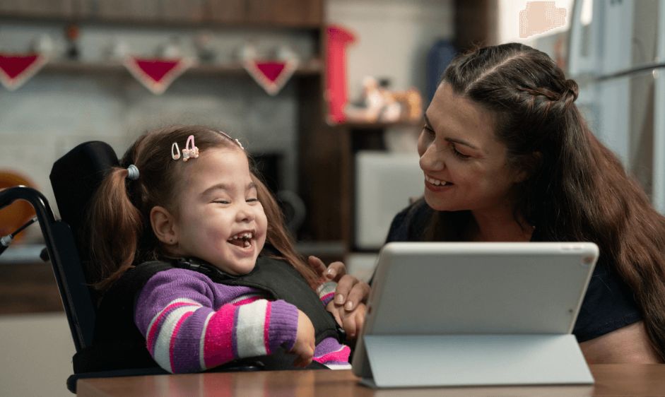 Little girl in wheelchair smiling at tablet with parent next to her