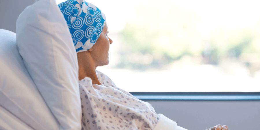 Woman wearing blue cap in hospital bed looking out window