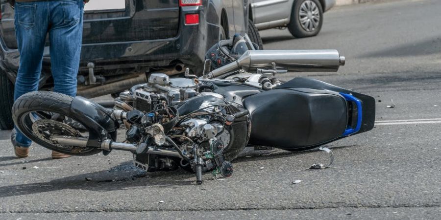 man walking away from crashed motorcycle on its side behind black suv