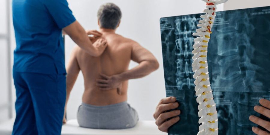 man gripping his back in pain with doctor examining him
