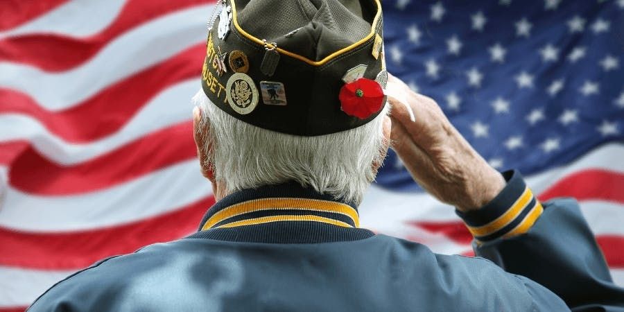 older man wearing veteran hat saluting american flag