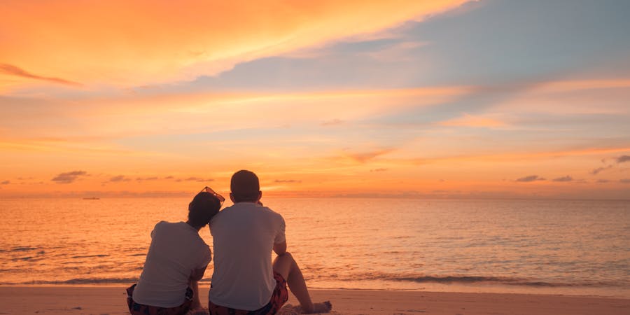 A couple sits together on a beach at sunset, creating a serene and reflective scene that underscores the importance of cherishing loved ones.