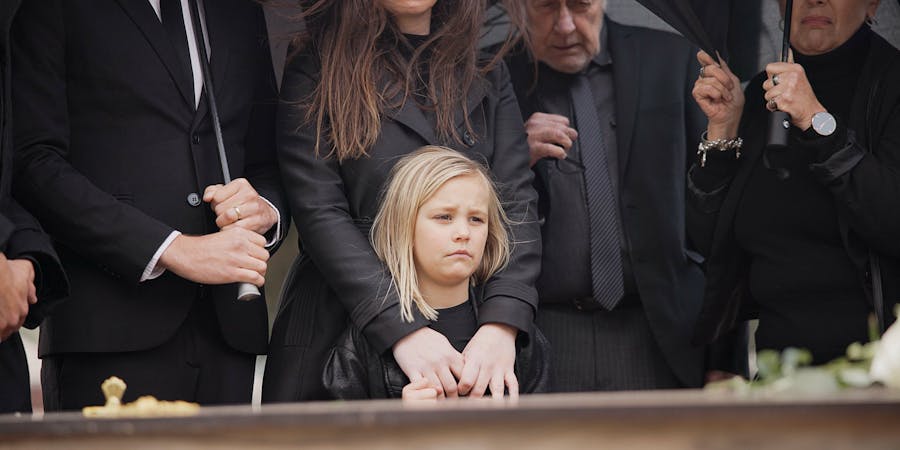 A grieving family, including a sad young girl, stands together under umbrellas at a funeral, highlighting the emotional impact of wrongful death