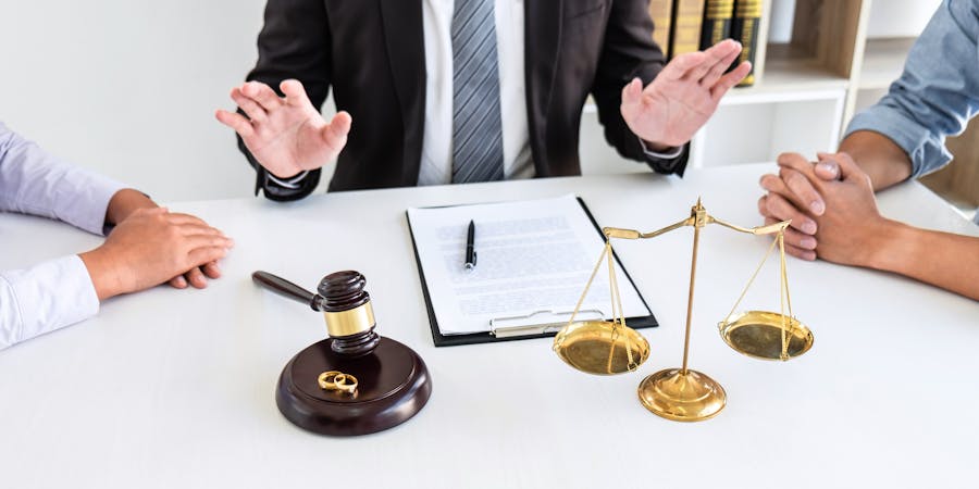 A gavel and scales of justice on a table with three people gesturing in conversation, suggesting a legal context.